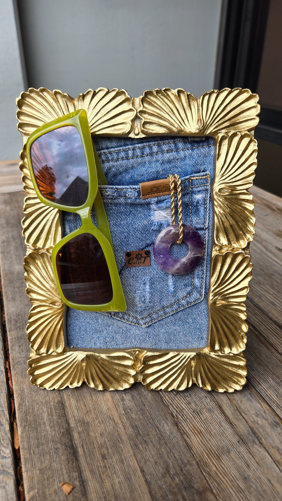 Gold shell frame denim pocket display with green glasses and purple pendant